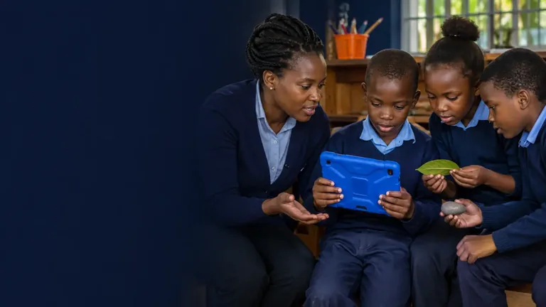 A teacher helping a small group of children use a tablet collaboratively.